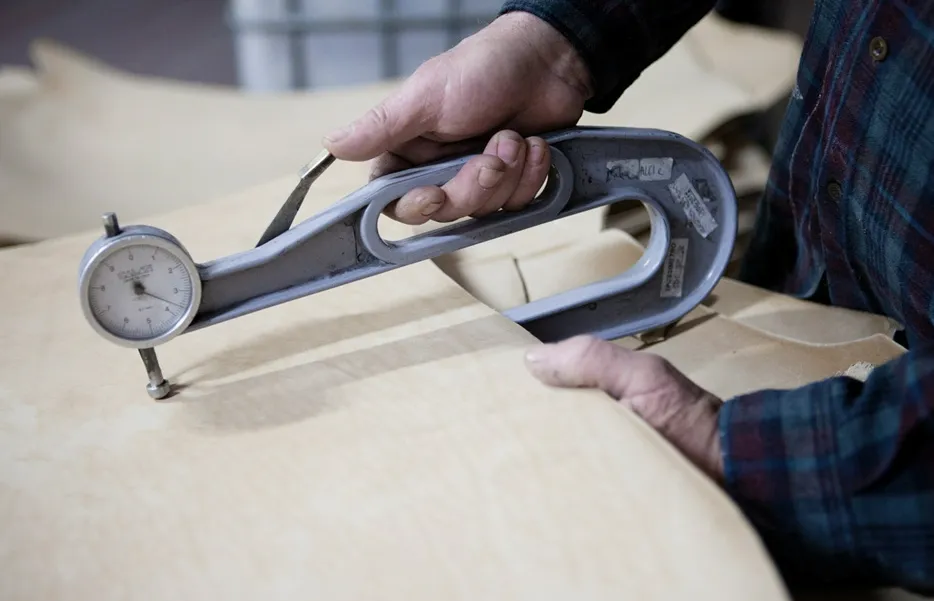 革1 職人が測定器具でレザーの厚さを正確に計測している様子。厳格な品質管理の一端を表しています。